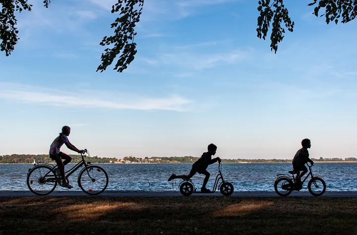 Tre barn cyklar längs en strand i skymningen.
