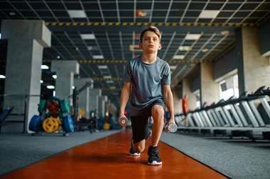 Bild på en ung pojke som tränar med hantlar på ett gym.