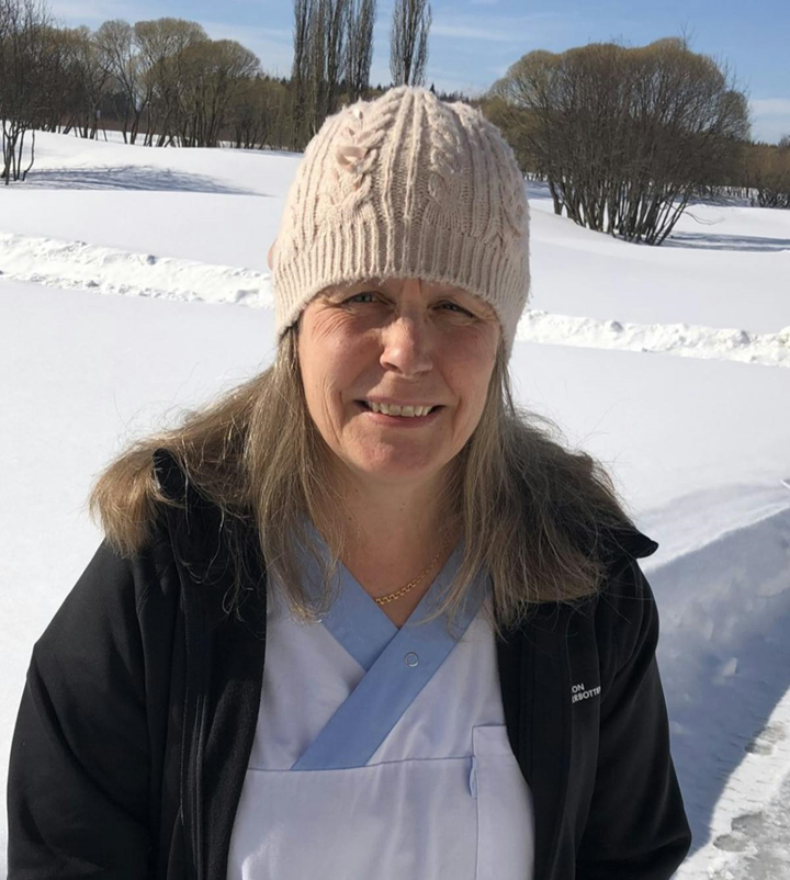 En bild på Anna Granström som står iklädd sjukhuskläder utomhus mot en snöig bakgrund.