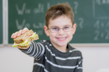 Pojke sträcker fram en smörgås mot kameran