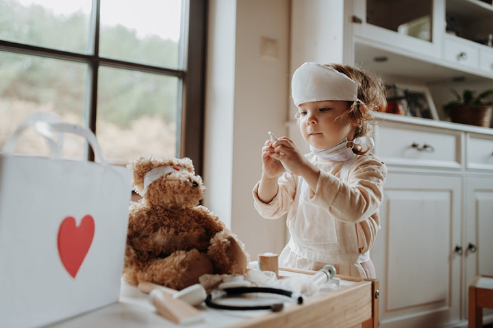 Bild på flicka utklädd till läkare med en teddybjörn som patient.