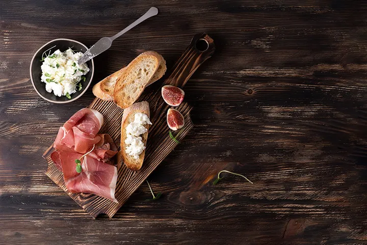 Träbricka med prosciutto, bröd med ost och fikon.