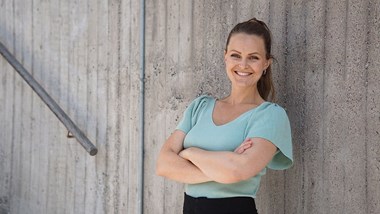 Stina står med armarna i kors lutad mot en grå stenvägg.