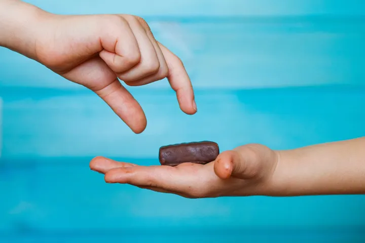Två händer. Den ena handen erbjuder en chokladbit till den andra handen.