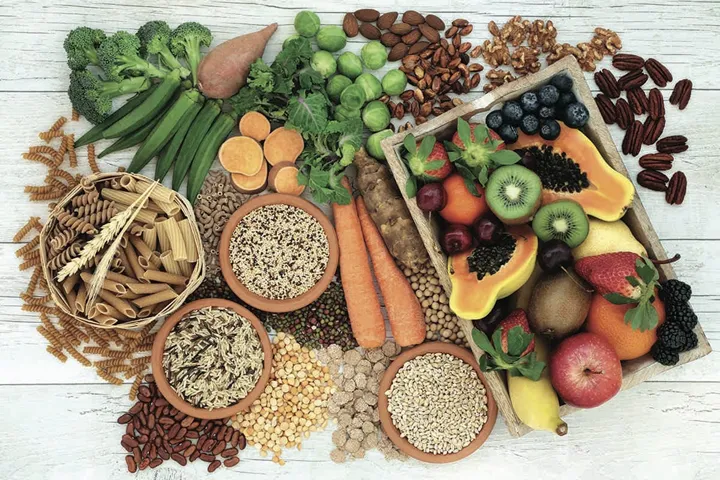 Health food for a high fiber diet with whole wheat pasta, grains, legumes, nuts, fruit, vegetables and cereals with foods high in omega 3 fatty acids, antioxidants and vitamins. Rustic background top view.