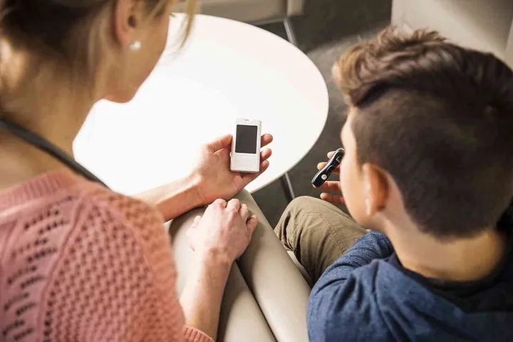 A female diabetes health care specialist with a young diabetes patient, testing his blood sugar levels.