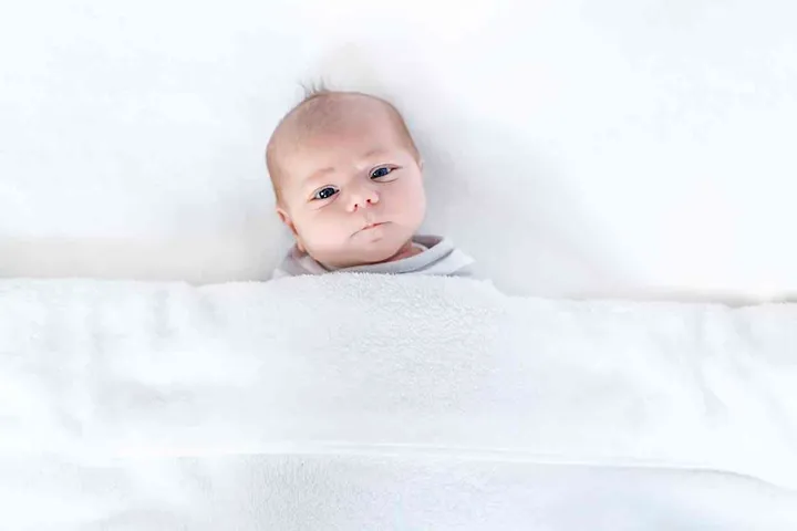 Cute adorable newborn baby in white bed and wrapped in blanket. New born child, little girl looking surprised at the camera. Family, new life, childhood, beginning concept.