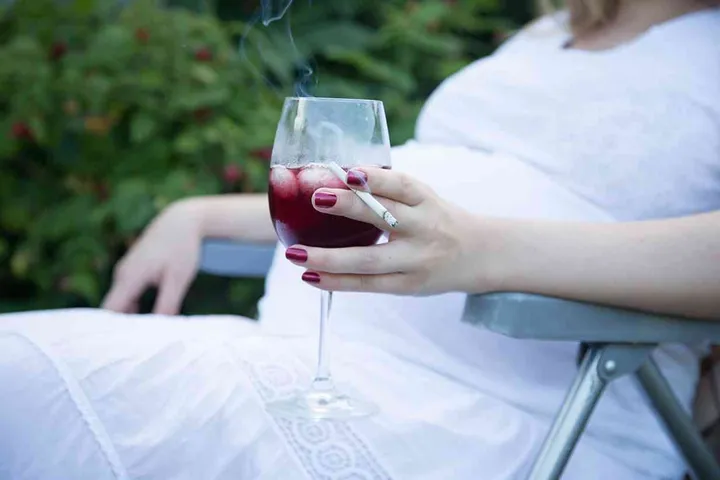 Young pregnant woman holding wine and cigarette